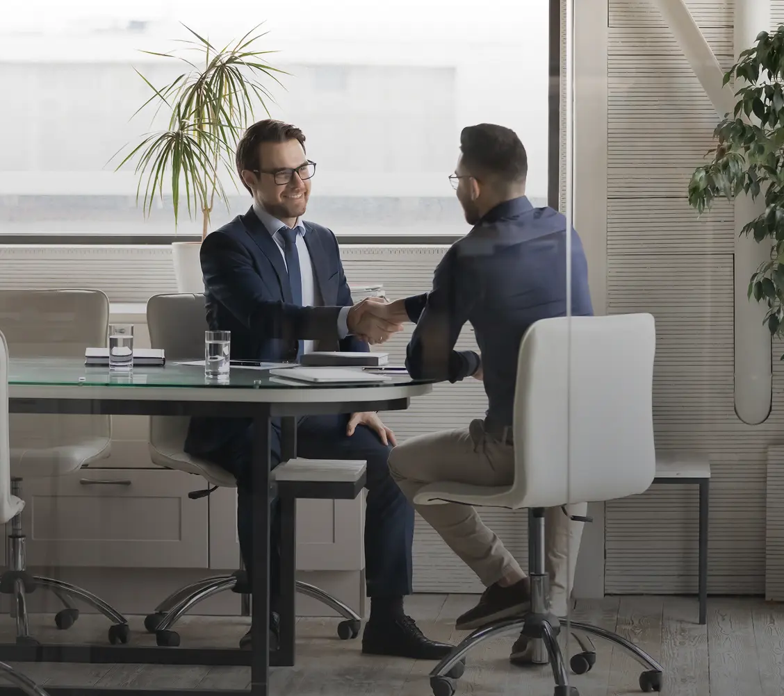 Deux hommes d'affaires en costume se serrant la main lors d'une réunion dans un bureau moderne avec une grande fenêtre.