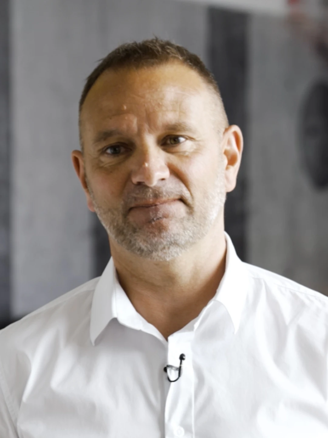 Homme avec barbe grise portant une chemise blanche, regardant la caméra avec un léger sourire.